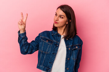 Young caucasian woman isolated on pink background joyful and carefree showing a peace symbol with fingers.