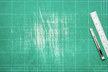 Top view of old green dirty cutting mat with stainless steel ruler and cutter knife, copy space for text and graphic.