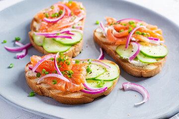 Toasts with cream cheese, smoked salmon, cucumber and red onion on rustic wooden table. Open sandwiches. Healthy care, super food concept.
