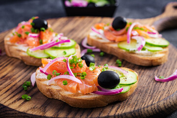 Toasts with cream cheese, smoked salmon, cucumber and red onion on dark  table. Open sandwiches. Healthy care, super food concept.