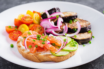 Delicious brunch  salmon  bread cream cheese sandwiches and arugula, tomatoes salad on a dark background.
