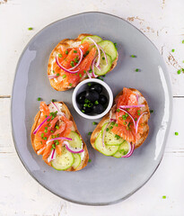 Toasts with cream cheese, smoked salmon, cucumber and red onion on rustic wooden table. Open sandwiches. Healthy care, super food concept. Top view, overhead