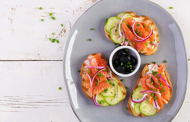 Toasts with cream cheese, smoked salmon, cucumber and red onion on rustic wooden table. Open sandwiches. Healthy care, super food concept. Top view, overhead