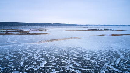 Winter landscape. Fishermen fish from the thin ice of a frozen reservoir. Ice flowers formed on the surface of the ice. Shooting from a drone.