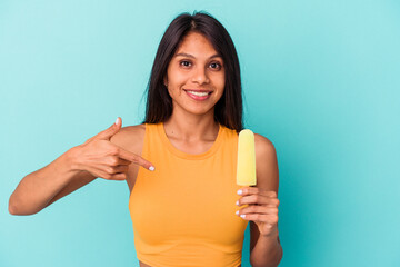 Young latin woman holding ice cream isolated on blue background person pointing by hand to a shirt copy space, proud and confident