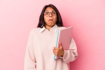 Young student latin woman isolated on pink background shrugs shoulders and open eyes confused.