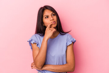 Young latin woman isolated on pink background looking sideways with doubtful and skeptical expression.