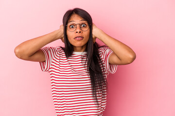 Young latin woman isolated on pink background covering ears with hands trying not to hear too loud sound.