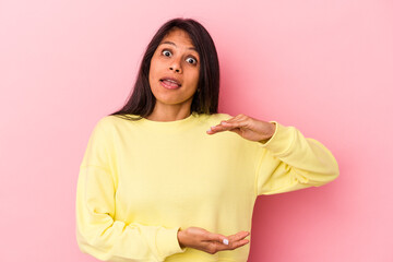 Fototapeta premium Young latin woman isolated on pink background holding something with both hands, product presentation.