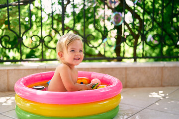 Smiling wet child sitting in a small inflatable pool with toys