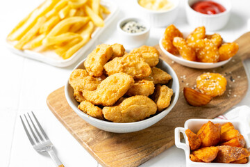 Chicken nuggets, strips, french fries, fried potatoes, ketchup and cheese sauce on a light background. Fast food closeup	