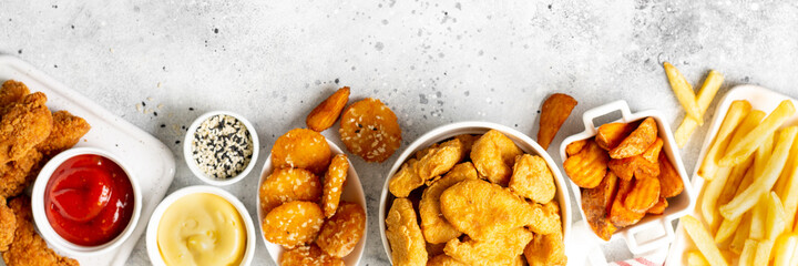 Chicken nuggets, strips, french fries, fried potatoes, ketchup and cheese sauce on a light background. Fast food top view with copyspace. Banner	