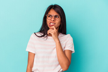 Young latin woman isolated on blue background touching back of head, thinking and making a choice.