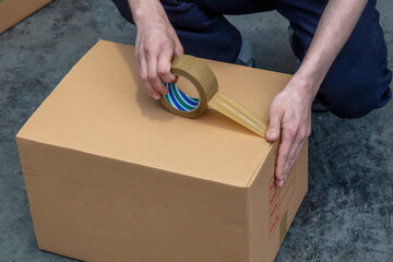 Packing Boxes with Tape. Sticking duct tape to a Kraft cardboard box. close-up of sealing cardboard...