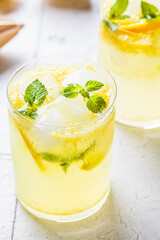 Homemade lemonade with mint and ice in glasses, gray tiles background.