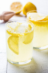 Homemade lemonade with ice in glasses, gray tiles background.