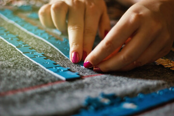Hand of a woman with nail polish playing Jigsaw Puzzle, starting to match the pieces to unveil the...