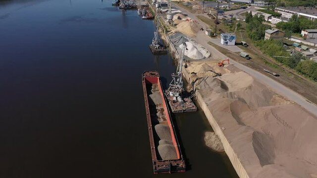 A harbor crane unloads a sand barge. Loading and unloading operations on the river. Aerial photography. . High quality FullHD footage