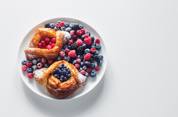 Danish with raspberries and blueberries on  round plate with berries on  white table