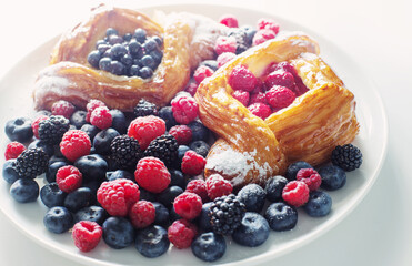 Danish with raspberries and blueberries on  round plate with berries on  white table