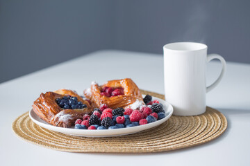 Danish with raspberries and blueberries with cup of tea on  white table