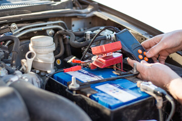 A man diagnoses a car battery with a tester, close-up. Battery repair and replacement