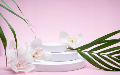 White geometric shapes podium for product display on pink background with orchid flowers and palm leaves. Monochrome stage, stand for product promotion in minimal style.
