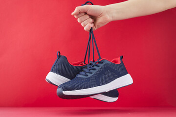 Hand hold sports shoes on red background. Holding new fashion sneakers for running. Choosing and...