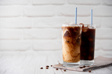 Iced coffee in a tall glass with cream on a white wood background. Cold tasty summer refreshment...
