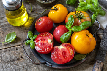 Fresh raw ripe organic yellow, red tomatoes and ingredients for cooking salad on a wooden table.