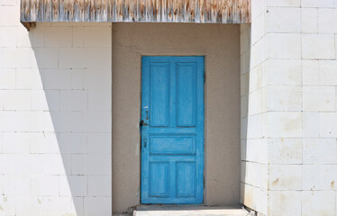 Older blue door in a white wall. The wall is made of light stone blocks.