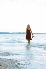 woman in black light dress walking barefoot by sea beach