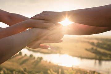 People's hands are folded on top of each other to develop the team and create a team against the background of the sky and the setting sun. The concept of unity, mutual support and mutual assistance.