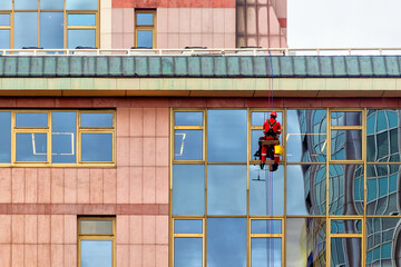 An industrial climber in a red uniform washes windows at a high altitude of an office building
