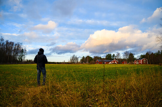 A scenic landscape view of open field filled with grass with red wooden cottages and rainbow in the sky in a rainy day during toristic outdoor visit