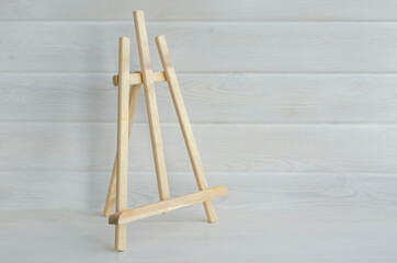 A small wooden easel on the background of a white wooden wall. Creative workshop, artist's workplace, art studio.