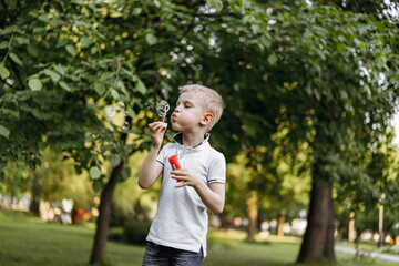 cute caucasian blond boy blowing soap bubbles in park