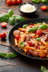 Sausage penne Pasta with tomato sauce, parmesan cheese and basil on black plate