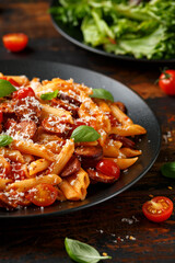 Sausage penne Pasta with tomato sauce, parmesan cheese and basil on black plate
