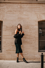 Gorgeous young brunette in midi slip dress, black oversized jacket and shoes posing outdoors...