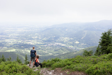 Fototapeta na wymiar Couple of two tourists, backpackers, hikers and trippers are having a rest and looking from lookout and outlook. Smrk, Beskid mountains, Czech Republic, Czechia. People in the nature.