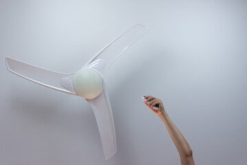 Close-up of hand holding remote control of white ceiling fan. Hand turning on the fan with copy space for text.