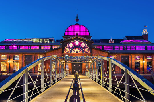 Hamburg, Germany - November 2, 2018: The historic fish auction hall (German: Fischauktionshalle), nowadays used as a venue in the harbor. At dusk it is colorfully illuminated.