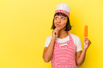 Young mixed race ice cream maker woman holding an ice cream isolated on yellow background looking sideways with doubtful and skeptical expression.