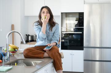 Young girl eating an apple sitting on the kitchen counter looking at the camera with expressions of surprise.