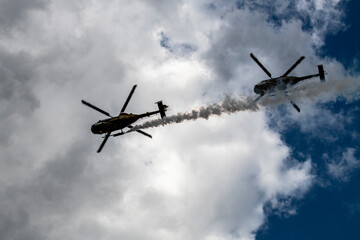 helicopters blow out a stream of smoke and make complex figures in flight against the background of the sky 