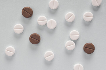 White and brown pills lie on a gray paper surface. Close-up. Light background or backdrop about medicine, health care, drugs, pharmacology. Tablets of different colors. Flat lay. Macro