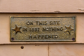 A sign reading "On This Site in 1897 Nothing Happened" is fastened to a wooden wall.