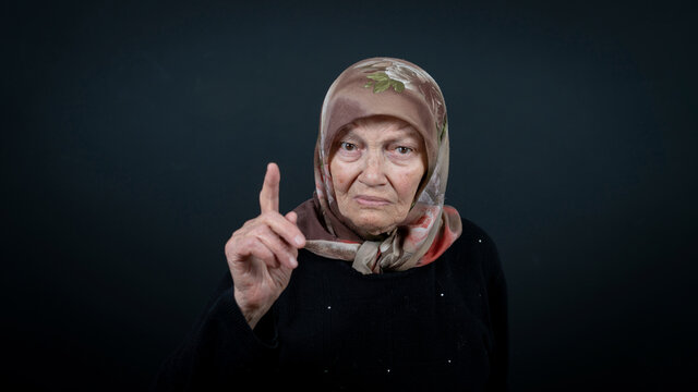 Portrait of a Turkish senior Muslim woman with black background. She has a angry expression on her face.