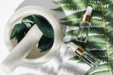 Natural herbal oils concept. Two bottles with essential oils lie on a palm leaf next to a mortar with herbs